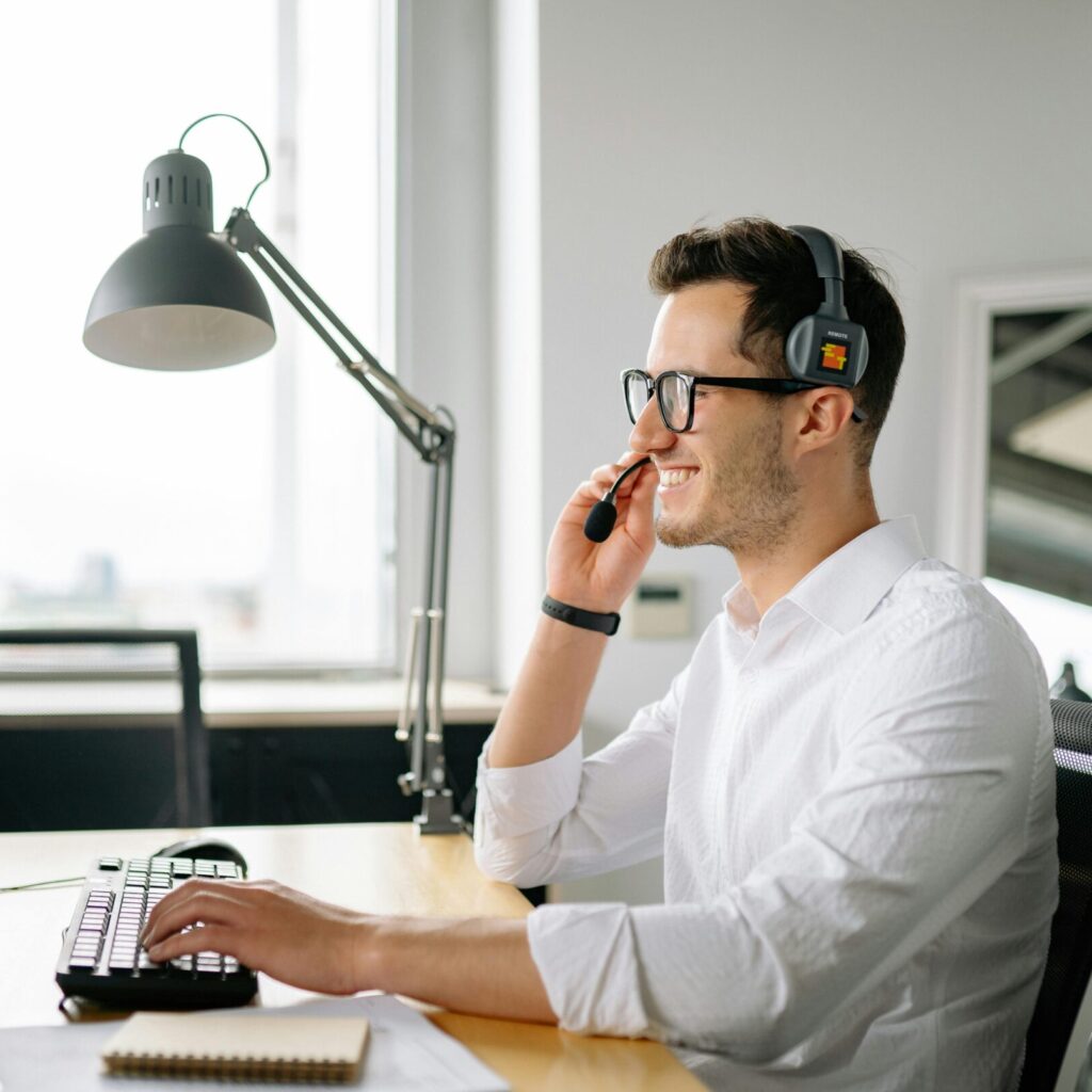Smiling man wearing headset working at computer in bright office.